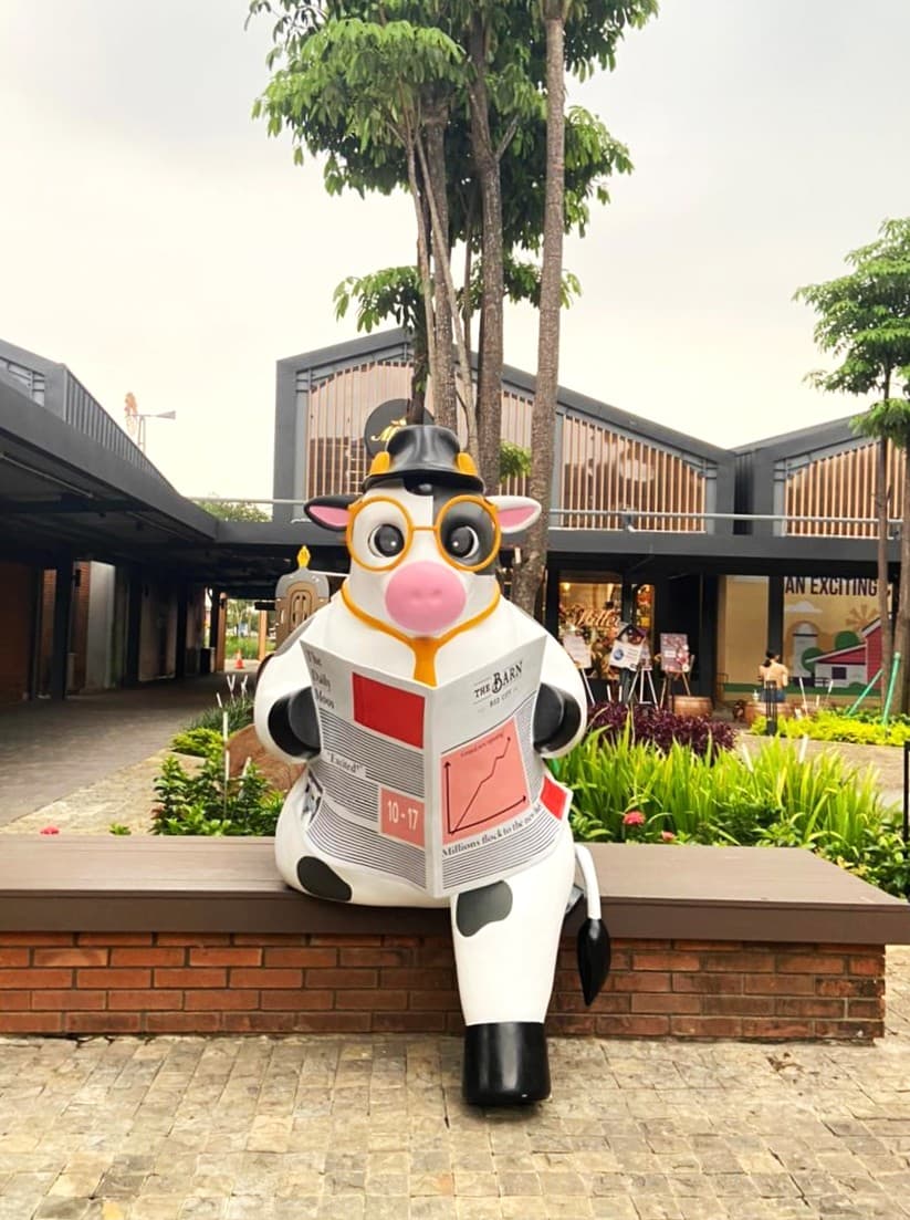 Giant cow statue in glasses and a bowler hat reading a newspaper on a bench at The Barn, BSD City, Indonesia